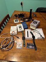 Overview of miscellaneous electronics and related items on table including Fitbit devices, boxes, cables, charging stand, and cards