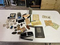 Wide view of all vintage items spread on a table showing various collectibles including badges, booklets, lighters, and ephemera.