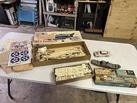 Overview photo showing table with model kits, parts laid out including box of SBD-3 Dauntless, steamboat model box, decals, and small white car model.