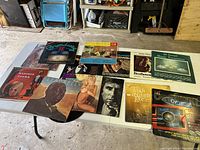 Photo of the entire lot showing 12 vintage LP albums laid out on a white table in a garage setting.