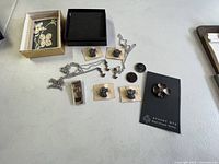 Photo showing assortment of sterling silver jewelry on a white surface including earrings on cards, a flower brooch card Stuart Nye, a rectangular pendant, cufflinks, and chains.
