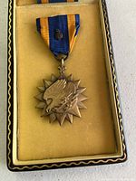 WWII American Air Medal with blue and orange ribbon displayed in original yellow fabric-lined black case with gold trim.