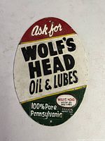 Oval vintage cast iron advertising sign for Wolf's Head Oil & Lubes with tri-color background and embossed text