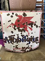 Full front view of sign leaning against background showing overall rust damage and porcelain loss.