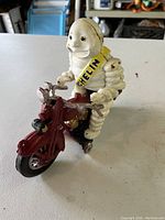 Front and side angle showing Michelin Man figure mounted on red motorcycle with Michelin sash.