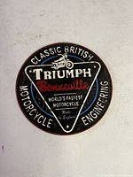 Front view of round cast iron Triumph Motorcycle Bonneville Flats sign showing painted raised lettering and motorcycle relief in black, white, red, and blue.