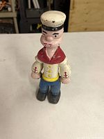 Front view of Popeye cast iron bank with visible paint wear, showing figure from front standing upright.