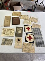 Collection of vintage wartime memorabilia laid out on a white table including ration books, stamps, photos, war insurance documents, and Red Cross insignia patches