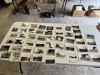Wide view of 50 black and white WWII Air Force crash photos laid out on a table showing various crash scenes and aircraft wreckage.
