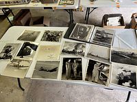 Overview of multiple vintage black and white WWII photos showing aircraft, personnel, and smoke or damage scenes on a folding table.