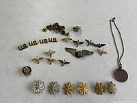 Wide view of entire collection showing rank insignias, US collar pins, pilot wings, clutch backs, and round pendant on chain.