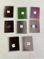 Backs of eight sleeved cards with various colored backing sleeves laid out on white surface
