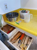 Angel food and Bundt pans, plastic measuring cup, container with cookie cutters, and kitchen drawers with rolling pins, utensils.