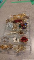 Photo showing 13 assorted vintage brooches and earrings including a large clear textured round brooch, gold-tone filigree brooch, multicolored stone floral brooch, and red rose enamel brooch
