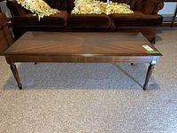 Front view of rectangular wooden coffee table with dark wood finish, turned legs and visible scratches.