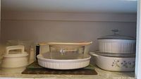 Wide photo showing multiple kitchenware items including Corningware casseroles, Pyrex bowl, plastic measuring cups, patty maker, and cutting boards.