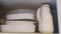 Three oval Corningware dishes stacked with a white Thermos carafe beside them
