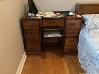Photo of the wood desk showing 8 drawers with metal pulls, and wood chair with upholstered seat positioned between the drawers, desk has scratches and signs of wear.