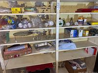 Six shelves stocked with disposable containers, lightbulbs in boxes, burner liners, and glass lids.