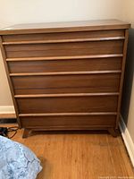 Front view of medium brown wood dresser with six drawers, light scratches visible on surfaces.