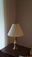 Single brass table lamp on wooden table, showing metal base and off-white fabric shade