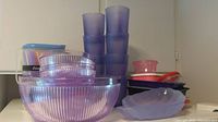 Various purple plastic bowls, cups, containers, straws and trays arranged on a countertop