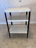 Full view of the three-tiered metal shelving unit showing its white shelves and black metal frame on floor.