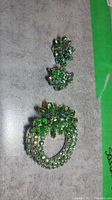 Green crystal clip-on earrings and green crystal circular brooch on gray surface
