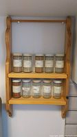 Front view of wooden wall mounted spice rack holding 10 glass spice bottles with lids and labels.