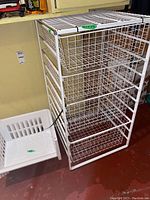 White metal wire storage unit with pull-out baskets alongside four white stackable plastic storage bins.