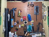 Pegboard wall holding various tools including caulking gun, wires, hand saws, tape, and extension cords.