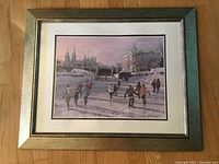 Framed print of canal ice skating scene with skaters and architectural background, on wooden floor.
