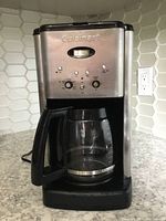 Front view of Cuisinart coffee maker showing stainless steel and black design, control buttons and glass carafe.