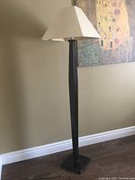Full view of floor lamp with dark brown wooden base and beige fabric lampshade