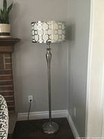 Chrome floor lamp against wall, lamp off showing geometric circle pattern on drum shade