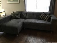 Front view of grey sectional sofa with chaise lounge and two pillows, showing wear and fabric texture.