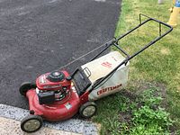 Side angle view of red Craftsman gas powered lawn mower with fabric grass catcher bag and black wheels on driveway