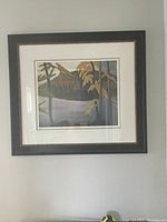 Framed print depicting a stylized lake landscape with tree branches in the foreground, hanging on a gray wall.