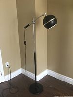 Full view of the floor lamp showing height, black base, adjustable arm, and spherical black head with chrome accents.