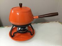 Front and side view of orange fondue pot on stand with wooden handle and burner under pot