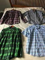 Four men's button-up shirts laid out on a bed showcasing the overall look and patterns of the shirts.