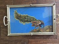 Front of the glass tray showing detailed peacock painting on blue background within metal frame and handles