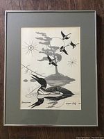 Front view of the framed black and white print featuring a loon, flying birds, a tree, and sun symbols.