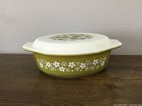 Oval casserole dish with lid. Side view showing olive green floral pattern on white glass.