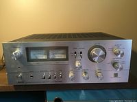 Front view of amplifier showing brushed aluminum faceplate, dual VU meters, control knobs and switches.