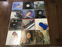 Photo showing 12 vinyl albums laid out on the floor in a 4 by 3 grid, covers visible showing various artists and artworks.