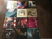 Photo showing 12 vinyl LP album covers arranged on a wooden floor. Various album cover arts in different colors and themes are visible.
