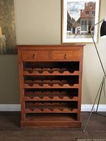 Front view of wooden wine cabinet showing two drawers and four shelves with curved slots for bottles.