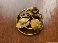 Brooch front view on wooden surface showing circular frame, rose and leaves