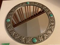 Full view of the round pewter mirror showing the leaf embossed frame and four turquoise colored stones.